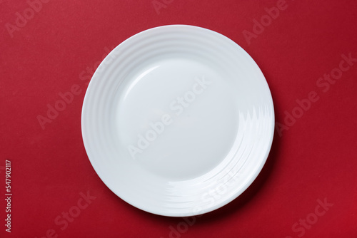 Empty white ceramic plate on red background, top view