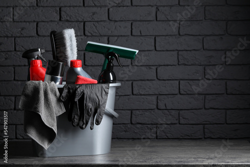 Different car cleaning products in bucket on table near black brick wall, space for text photo