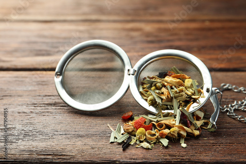 Snap infuser with dried herbal tea leaves on wooden table, closeup