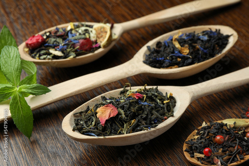 Spoons with dried herbal tea leaves on wooden table, closeup