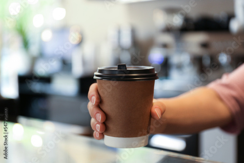 Barista putting takeaway paper cup with coffee on countertop in cafe, closeup