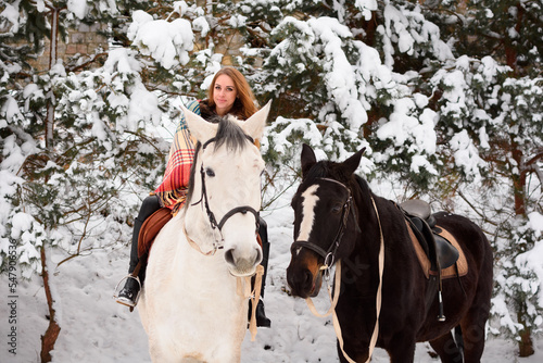 Red-haired girl on a horse in winter in the forest. Everything around is white. Christmas atmosphere around the world. Copy space