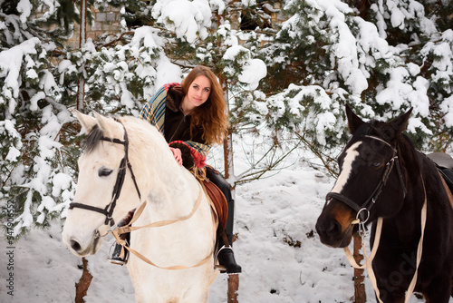 Red-haired girl on a horse in winter in the forest. Everything around is white. Christmas atmosphere around the world