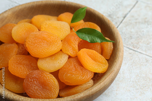 Wooden bowl of tasty apricots on white tiled table, closeup. Dried fruits