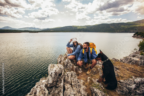 Hikers with backpacks and their doberman  sitting on cliff enjoying at the mountain lake © Mediteraneo