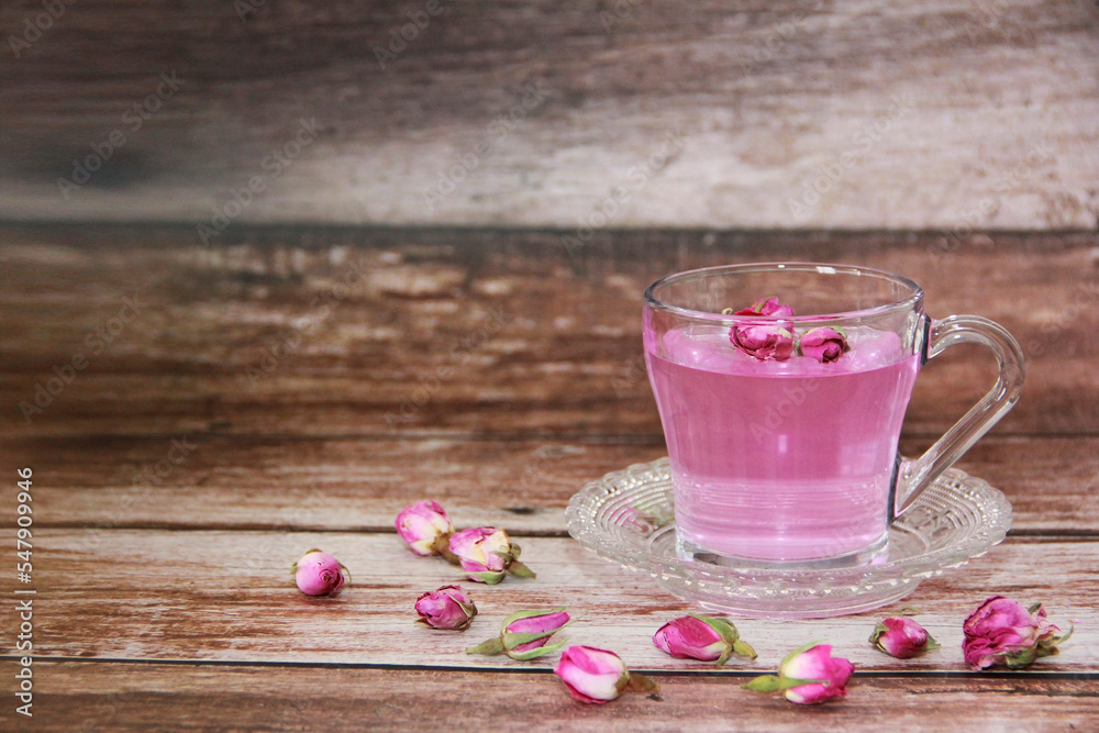 pink tea in a transparent glass mug with small dry buds of natural roses on a wooden background pink tea in a transparent glass mug with small dry buds of natural roses on a wooden background