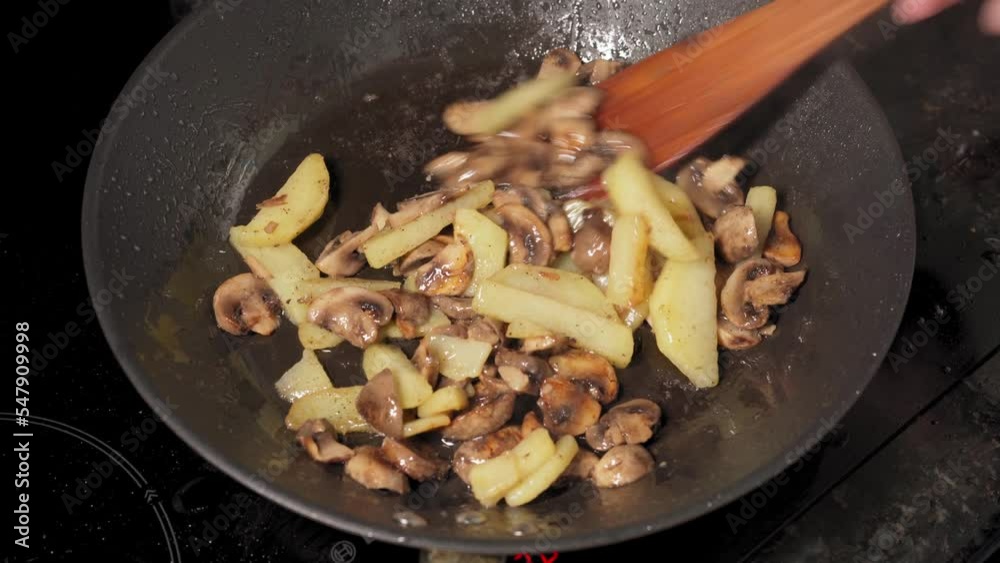 Frying Mushrooms and Potatoes Pieces in a Hot Frying Pan, Baking Champignons Cuts, Cooking Food, Roasting Mushrooms and Potatoes, Mixing with a Wooden Spatula Frying Mushrooms and Potatoes Pieces in a Hot Frying Pan, Baking Champignons Cuts, Cooking Food, Roasting Mushrooms and Potatoes, Mixing with a Wooden Spatula