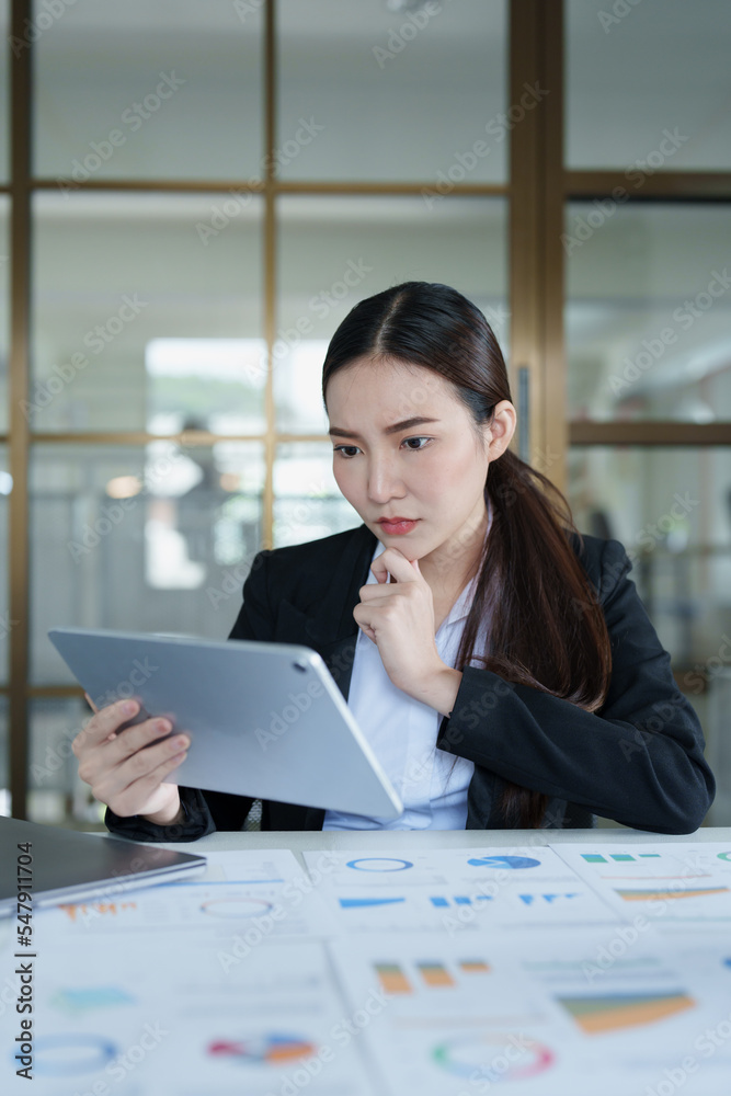 Portrait of a thoughtful Asian businesswoman looking at financial statements and making marketing plans using a tablet computer on her desk Portrait of a thoughtful Asian businesswoman looking at financial statements and making marketing plans using a tablet computer on her desk