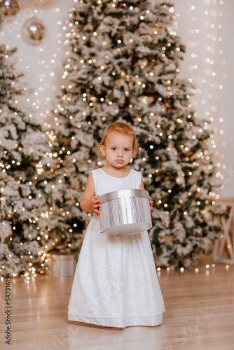 Girl in white evening dress is posing with silver present in Christmas studio