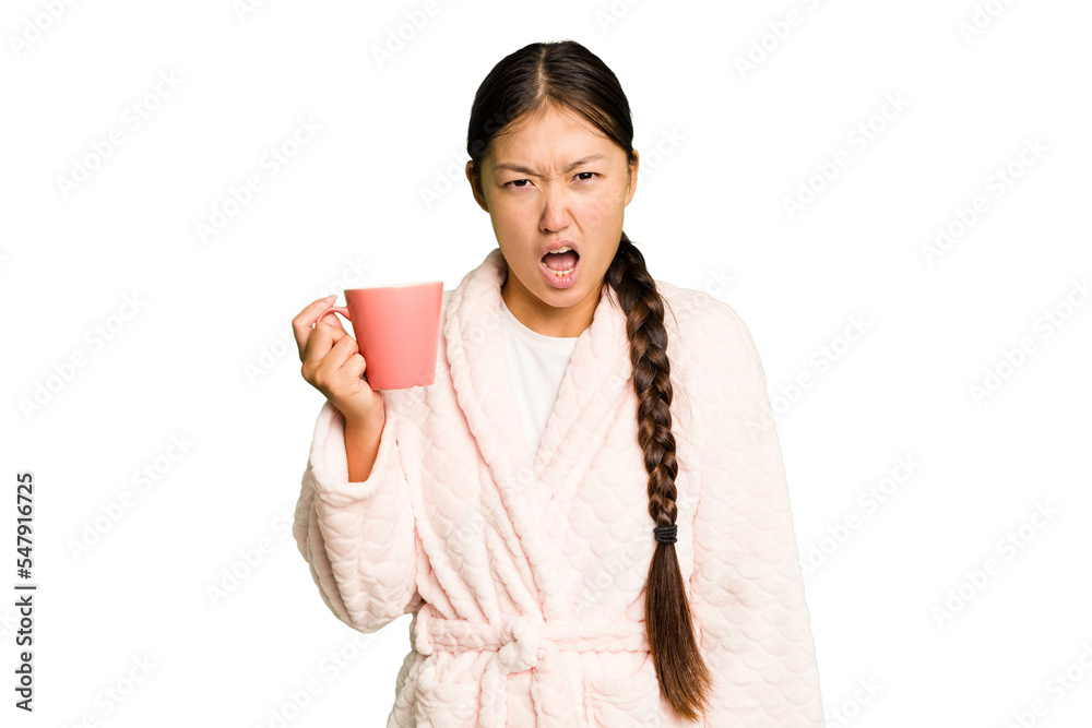 Young asian woman wearing a pajama holding a cup isolated screaming very angry and aggressive. Young asian woman wearing a pajama holding a cup isolated screaming very angry and aggressive.
