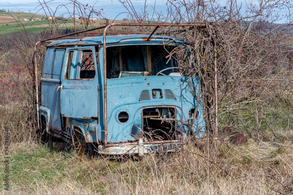 veille voiture bleue rouillée abandonnée dans un champ avec la végétation la recouvrant depuis des années au bord d'un chemin de randonnée dans le puy de dôme