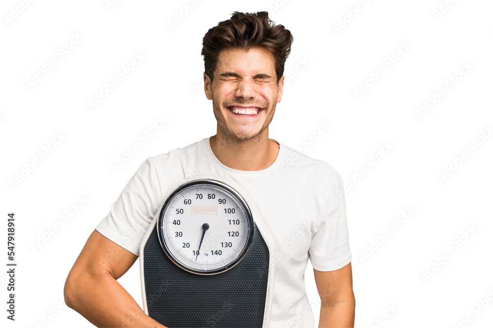 Young caucasian man holding a scale isolated laughing and having fun. Young caucasian man holding a scale isolated laughing and having fun.