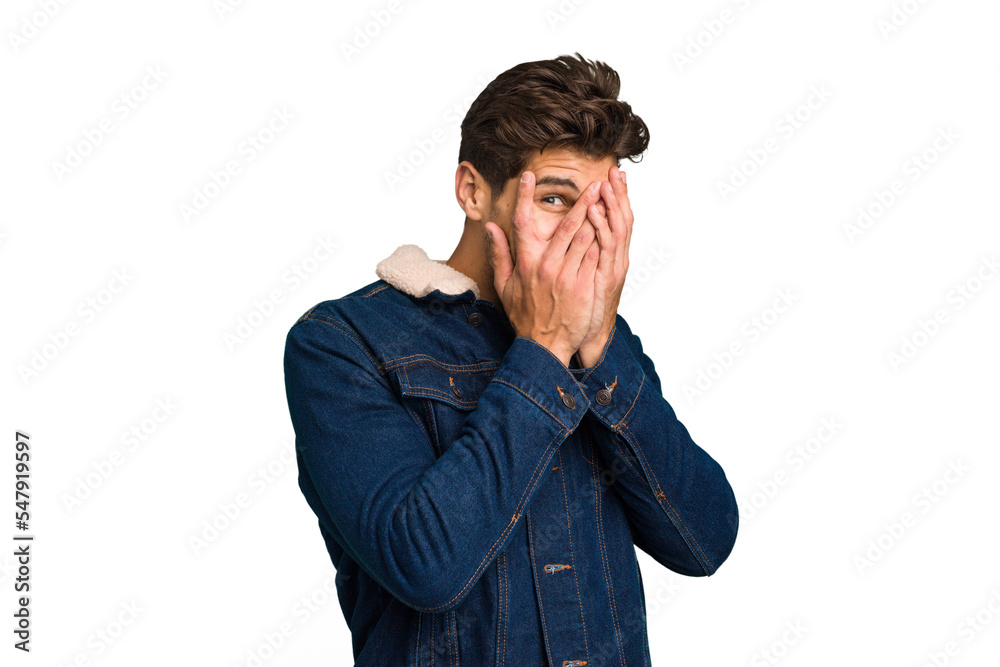 Young caucasian handsome man isolated blink at the camera through fingers, embarrassed covering face. Young caucasian handsome man isolated blink at the camera through fingers, embarrassed covering face.