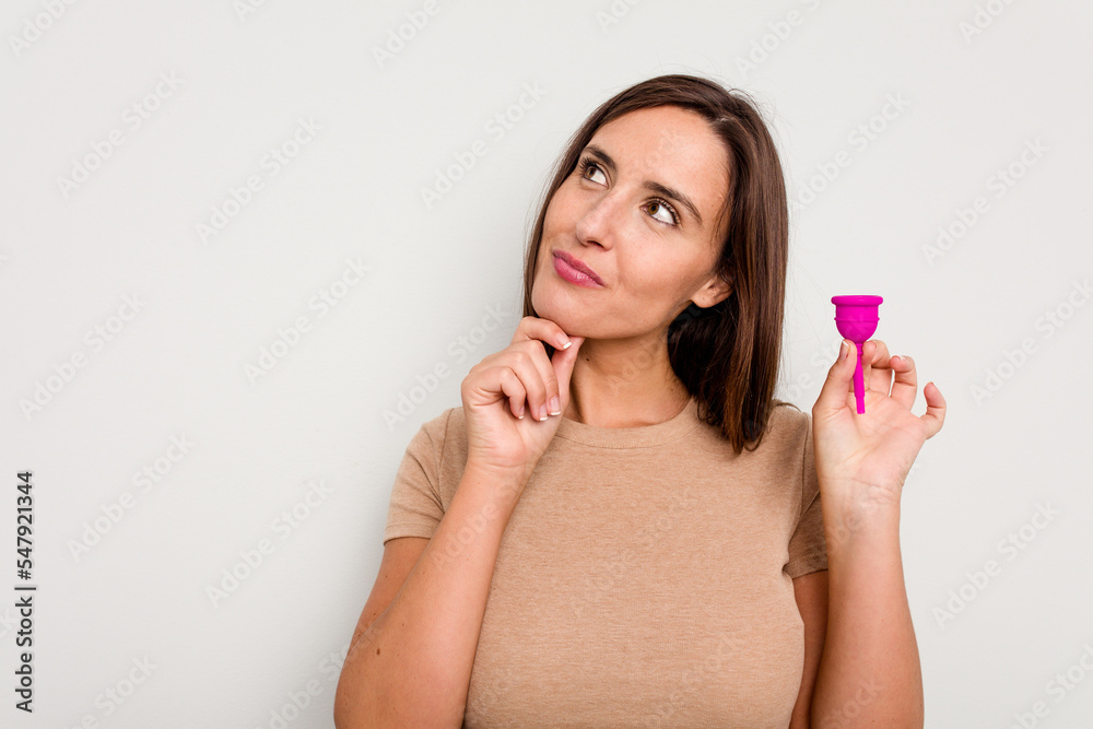 Young caucasian woman holding menstrual cup isolated on white background looking sideways with doubtful and skeptical expression. Young caucasian woman holding menstrual cup isolated on white background looking sideways with doubtful and skeptical expression.