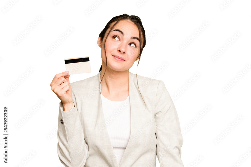 Young caucasian woman holding a credit card isolated on green chroma background dreaming of achieving goals and purposes Young caucasian woman holding a credit card isolated on green chroma background dreaming of achieving goals and purposes