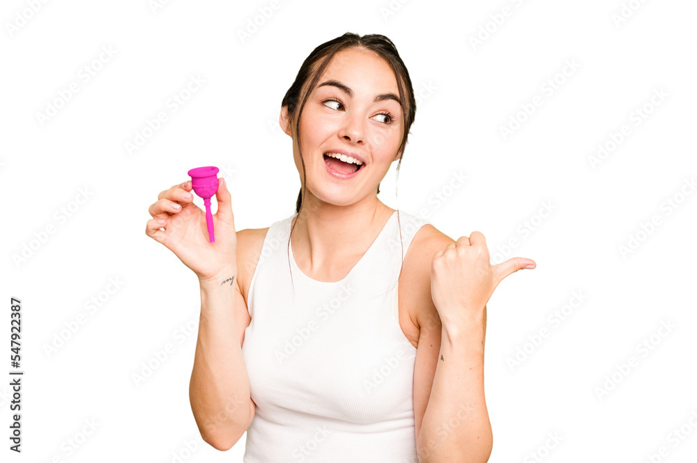 Young caucasian woman holding menstrual cup isolated on green chroma background points with thumb finger away, laughing and carefree. Young caucasian woman holding menstrual cup isolated on green chroma background points with thumb finger away, laughing and carefree.
