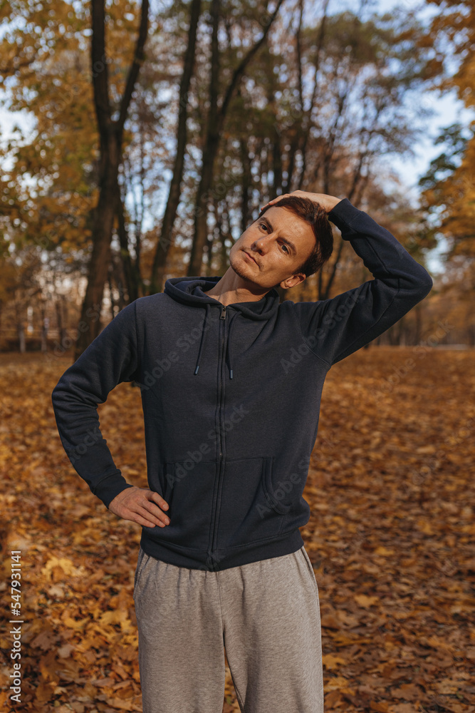 Athletic male runner warming up neck or head while exercising during training on sunny day in autumn park Athletic male runner warming up neck or head while exercising during training on sunny day in autumn park
