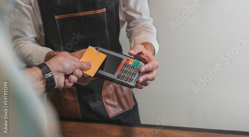 Detalle de mano, de cliente pagando con tarjeta bancaria, en el datafono al irreconocible peluquero, en la peluquería. 