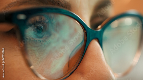 Macro of female hacker eyes. Reflection of screen computer lights on programmer eyeglasses. Female using internet, reading, watching, styding, analizing, working online late. photo