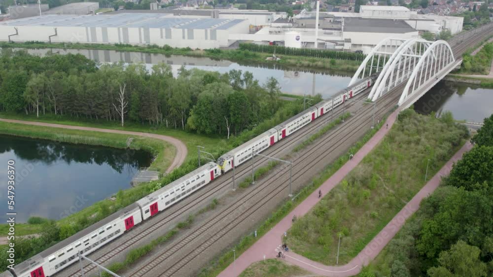 Aerial view shot by a drone of a train passing by on the railway track and over a bridge across a river in Belgium . High quality 4k footage