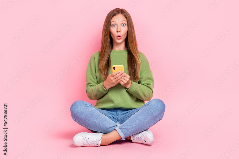 Full length photo of cute impressed schoolgirl wear green sweatshirt reading messages modern gadget isolated pink color background Full length photo of cute impressed schoolgirl wear green sweatshirt reading messages modern gadget isolated pink color background