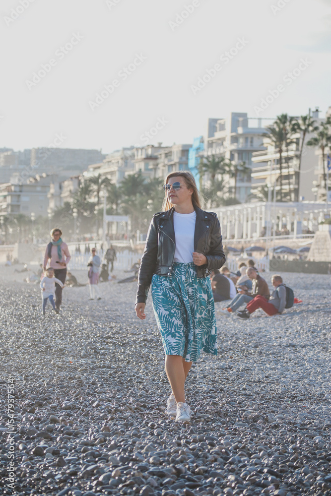Fototapeta premium Young beautiful girl on an autumn sunny day walks on the beach of the Mediterranean Sea