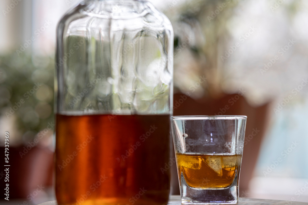 Whiskey glass with ice cubes, misted bottle on wooden table