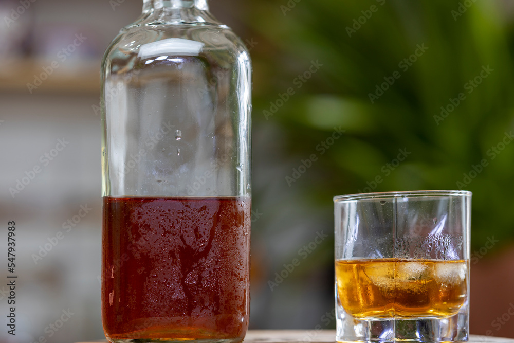 Glass of whiskey on ice with bottle on wooden bar Glass of whiskey on ice with bottle on wooden bar