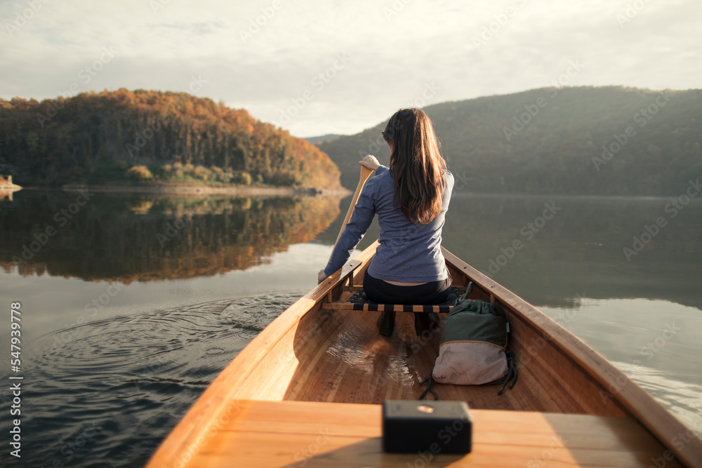 Rear view of woman paddling canoe on autumn lake