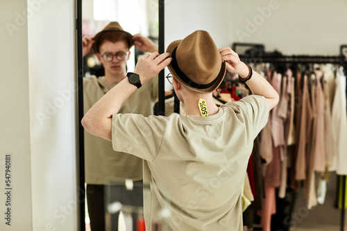 Back view of young man trying on hat in thrift store and looking in mirror, focus on sale tag, copy space photo