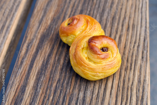 A homemade saffron bun lies on a piece of textured wood.  photo