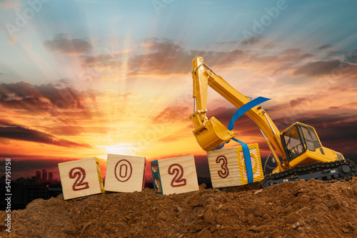Concept Happy new year 2023,crawler excavator of lift up bucket that is installing the number three in construction site .with sunset backgrounds