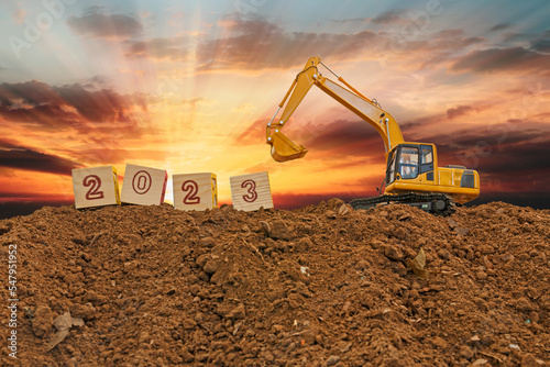 Concept Happy new year 2023,With Crawler excavator lift up bucket in construction site .On Sunset backgrounds