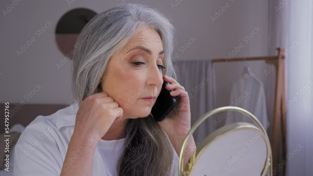 Talking phone speaking mobile talk senior gray-haired old 60s woman lady looking at mirror reflection touching face wrinkled skin speak remote conversation aging perfect smooth skincare moisturizing Talking phone speaking mobile talk senior gray-haired old 60s woman lady looking at mirror reflection touching face wrinkled skin speak remote conversation aging perfect smooth skincare moisturizing