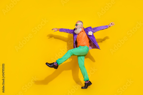 Full length photo of positive funky man wear purple velvet jacket walking hands sides discotheque isolated yellow color background © deagreez