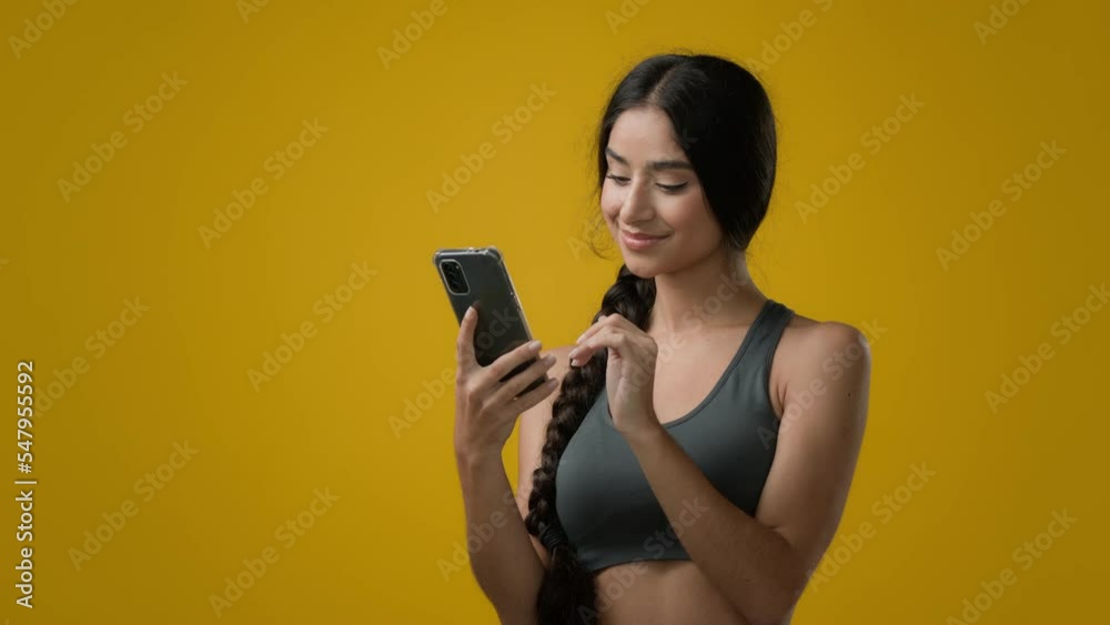Female in studio yellow background Indian 20s sporty woman athlete girl in sportswear lady with smartphone browsing typing scrolling chat in Internet online workout sport chatting with mobile phone Female in studio yellow background Indian 20s sporty woman athlete girl in sportswear lady with smartphone browsing typing scrolling chat in Internet online workout sport chatting with mobile phone
