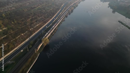 Train driving on railway along Elbe river and road near Melnik city in Czech Republic, drone following evening view photo