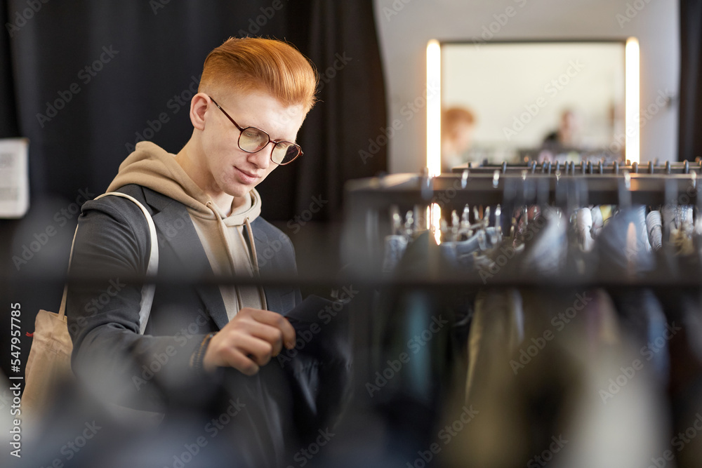 Waist up portrait of stylish young man looking at clothes while shopping sustainably in thrift store, copy space