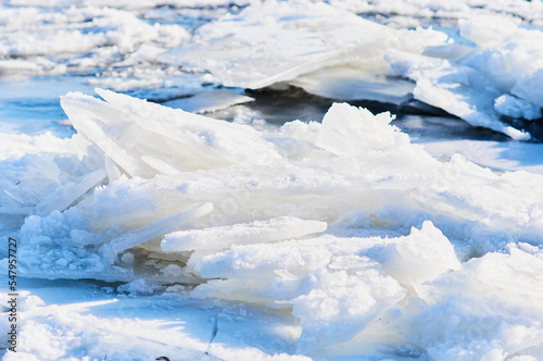 Ice floes float on the river. Seasonal ice drift. Natural texture. Bright sunlight and shadows from a heap of ice blocks.