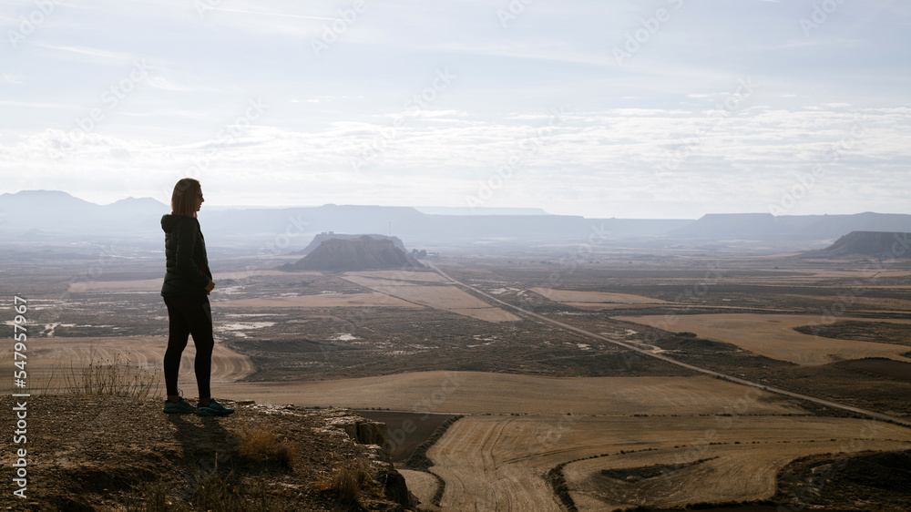 Silhouette of a woman in profile observing the arid desert plain from the top. Desert with gully mountains and sandstone plateaus.