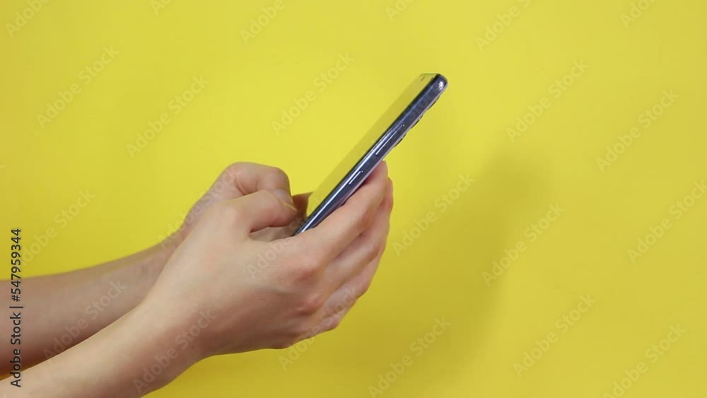 Woman using smartphone on yellow background. Hand holding mobile phone on chroma key background. Technology addiction concept. Messaging or online ordering. Woman using smartphone on yellow background. Hand holding mobile phone on chroma key background. Technology addiction concept. Messaging or online ordering.