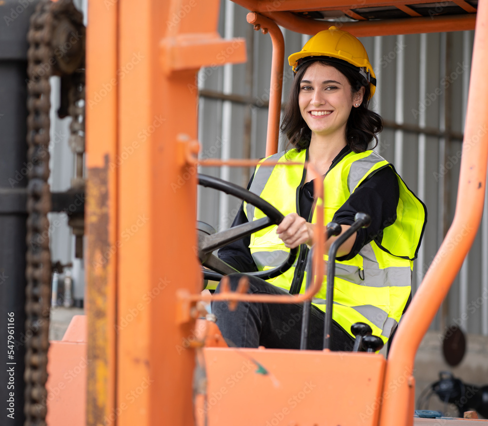 Female foreman wears hard hat driving forklift at shipping container ...