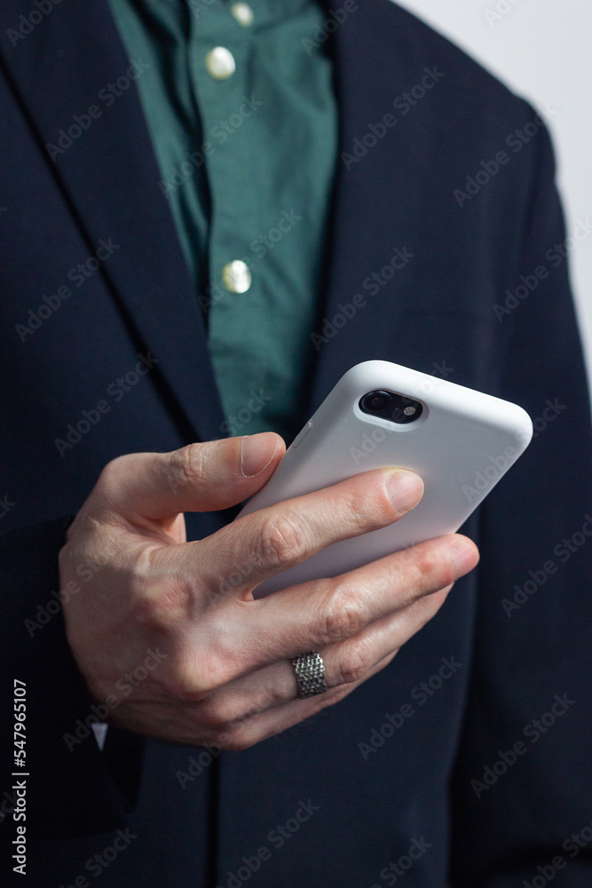 Male hands of a businessman in a business suit with a ring on his finger hold a modern gadget, a phone in a white case in his hands. Vertical orientation photo, business style.