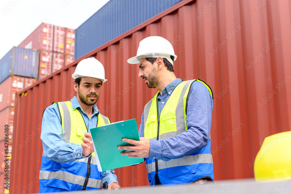 Supervisor and colleagues in white hard hats and safety vests stand in front of container box and talk about logistics operations. Transportation import and export logistic industry concept. Supervisor and colleagues in white hard hats and safety vests stand in front of container box and talk about logistics operations. Transportation import and export logistic industry concept.