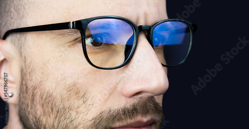 The face of a young man in glasses looking at the monitor. Close-up. Banner. Copy space. Selective focus.
