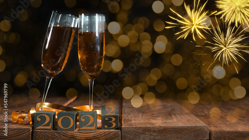 New Year New Year's Eve celebration holiday greeting card background - Cubes with change of year from 2022 to 2023 and sparkling wine or champagne glasses toasting on table and fireworks on sky