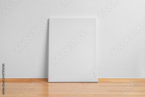 Clean art canvas leaning against a white wall. Parquet floor with reflection