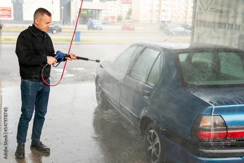 Car wash or cleaning with high pressure water using foam. Hand washing the car with water.  A man washes his car at a self-service car wash. © Pokoman