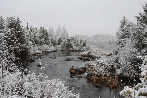 Winter Scenery Season Photo and Image. Horizontal Photo. Displaying its white blanket on trees, river and with a grey sky with a tranquillity feeling of peace.
