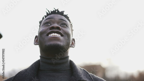 Hopeful black man opening eyes to sky smiling